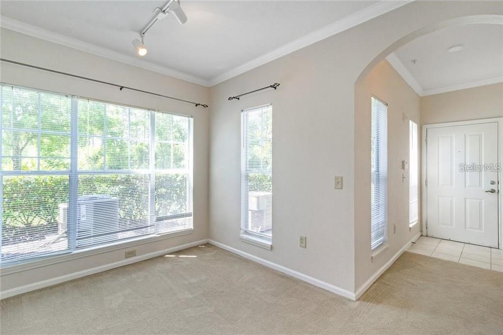 An empty room with beige carpet, light-colored walls, large windows, and a white front door — 11702 HERITAGE ESTATES AVE UNIT 318, ORLANDO, FL