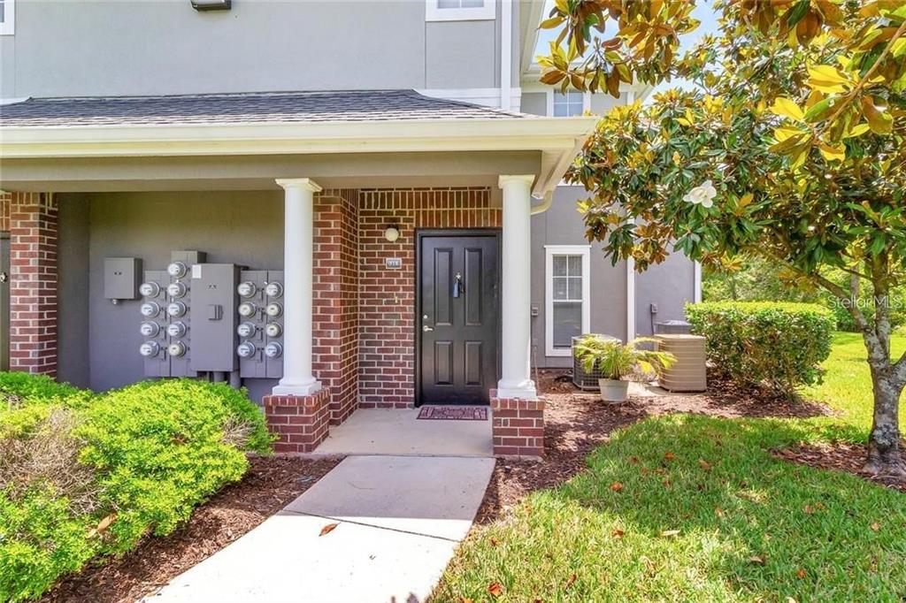 A covered porch with brick columns leads to a black front door of a townhouse — 11702 HERITAGE ESTATES AVE UNIT 318, ORLANDO, FL