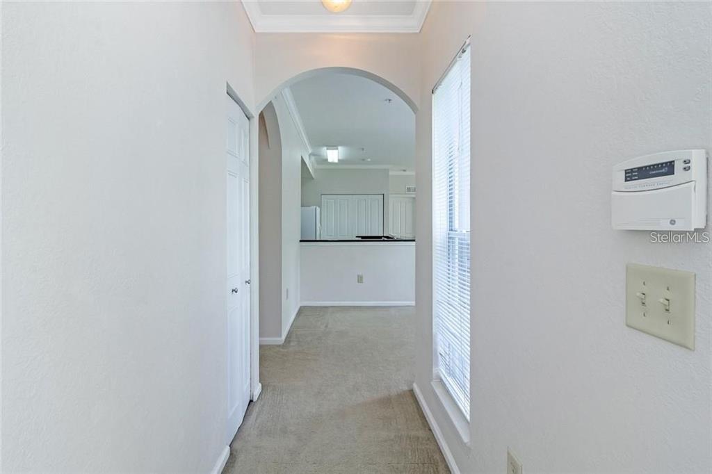 A carpeted hallway leads through an arched doorway toward a kitchen with white cabinets — 11702 HERITAGE ESTATES AVE UNIT 318, ORLANDO, FL