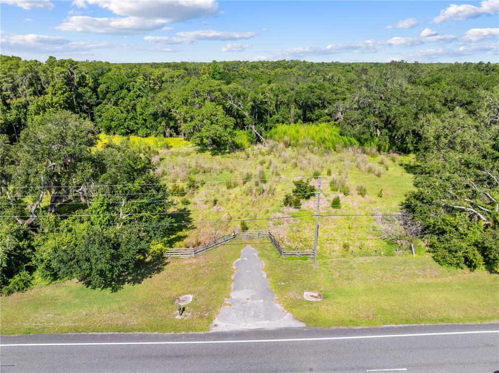 An aerial view shows a paved driveway leading to a fenced, grassy lot with trees — PLEASANT HILL RD ROAD, KISSIMMEE, FL
