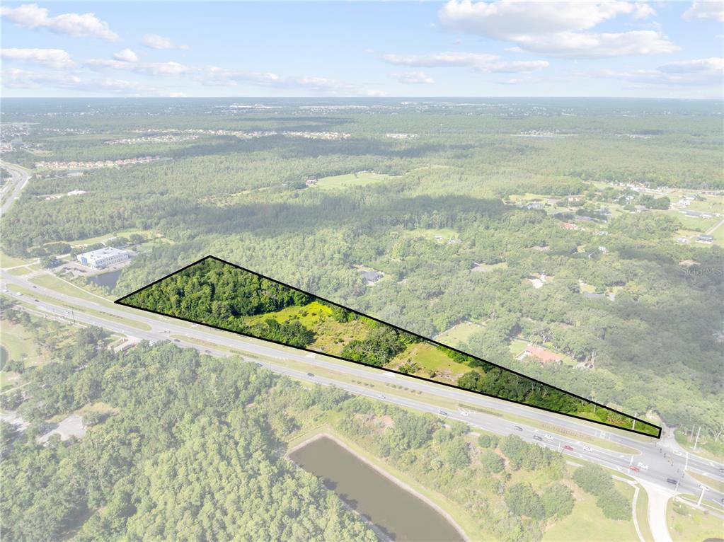 An aerial view shows a triangular plot of undeveloped land bordering a multi-lane highway — PLEASANT HILL RD ROAD, KISSIMMEE, FL