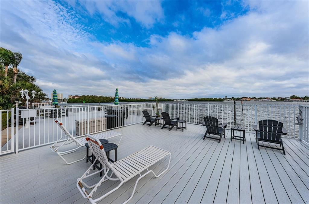 A spacious wooden deck overlooks a body of water with various outdoor seating options — 1859 SHORE DRIVE S UNIT 107, SOUTH PASADENA, FL