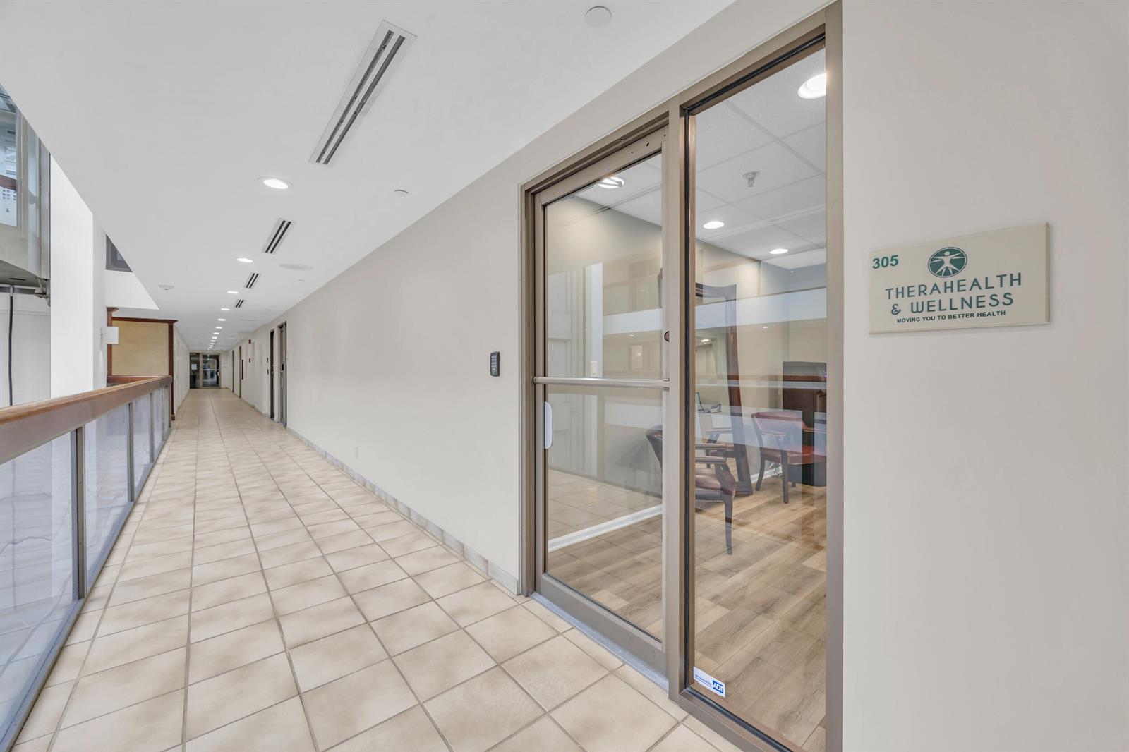 A hallway with tiled flooring leads to a glass-fronted office suite labeled Therahealth & Wellness — 631 Us-1, North Palm Beach FL 33408, NORTH PALM BEACH, FL