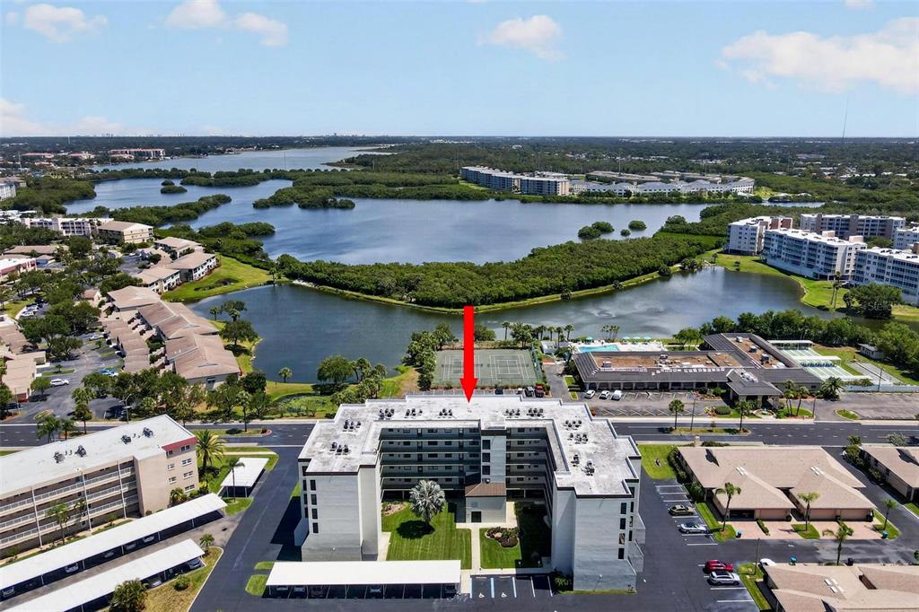 An aerial view shows a multi-story apartment building with a red arrow pointing toward it — 9860 62ND TERRACE N UNIT 1043, ST PETERSBURG, FL