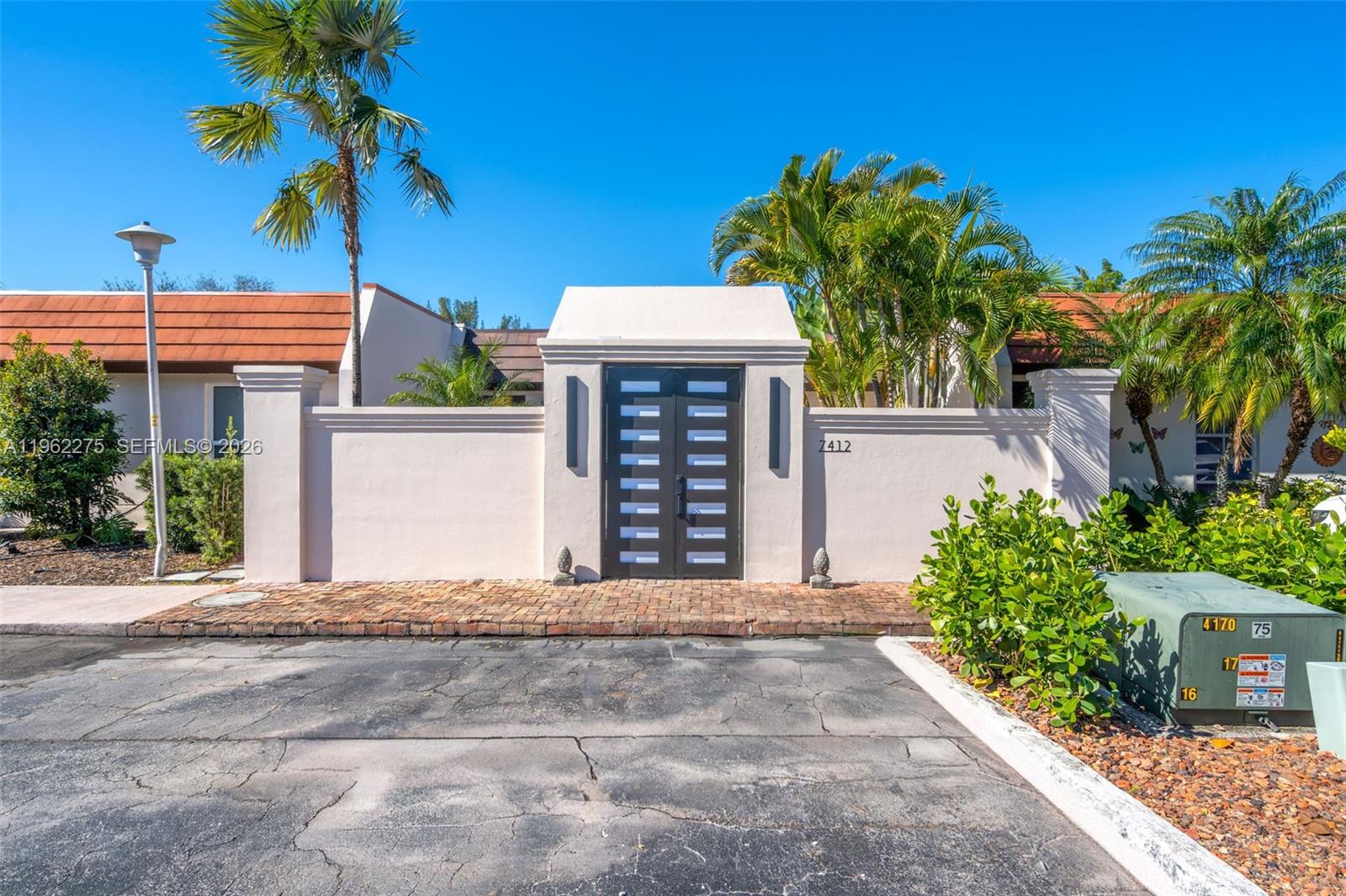 A gated entrance with double doors sits in a stucco wall before a residential building — 7412 Big Cypress Dr, Miami Lakes FL 33014, MIAMI LAKES, FL