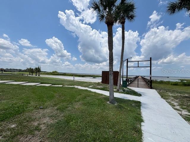 A concrete path leads to a wooden pier extending into a lake under a cloudy sky — 3041 AZALEA DRIVE, INDIAN LAKE ESTATES, FL