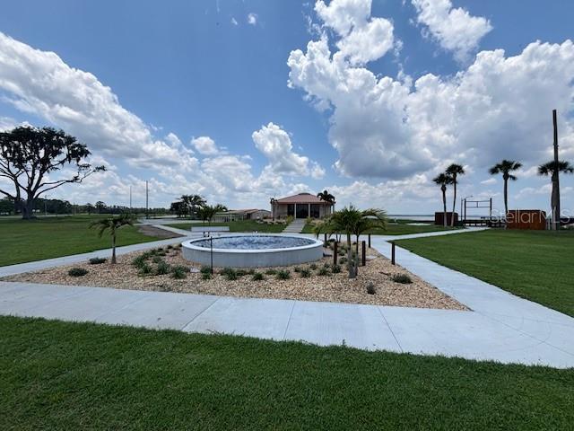 A circular fountain sits in a landscaped courtyard with palm trees and a building behind — 3041 AZALEA DRIVE, INDIAN LAKE ESTATES, FL