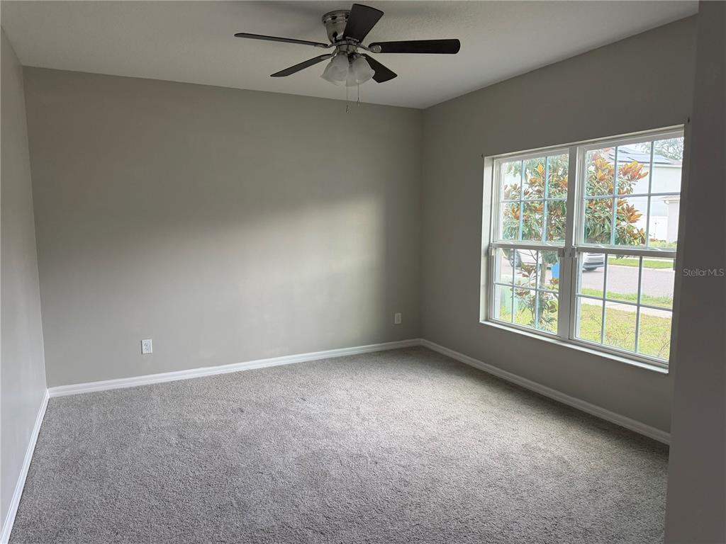 An empty bedroom features gray walls, gray carpeting, a ceiling fan, and a large window — 911 AVENAL LANE, DAVENPORT, FL