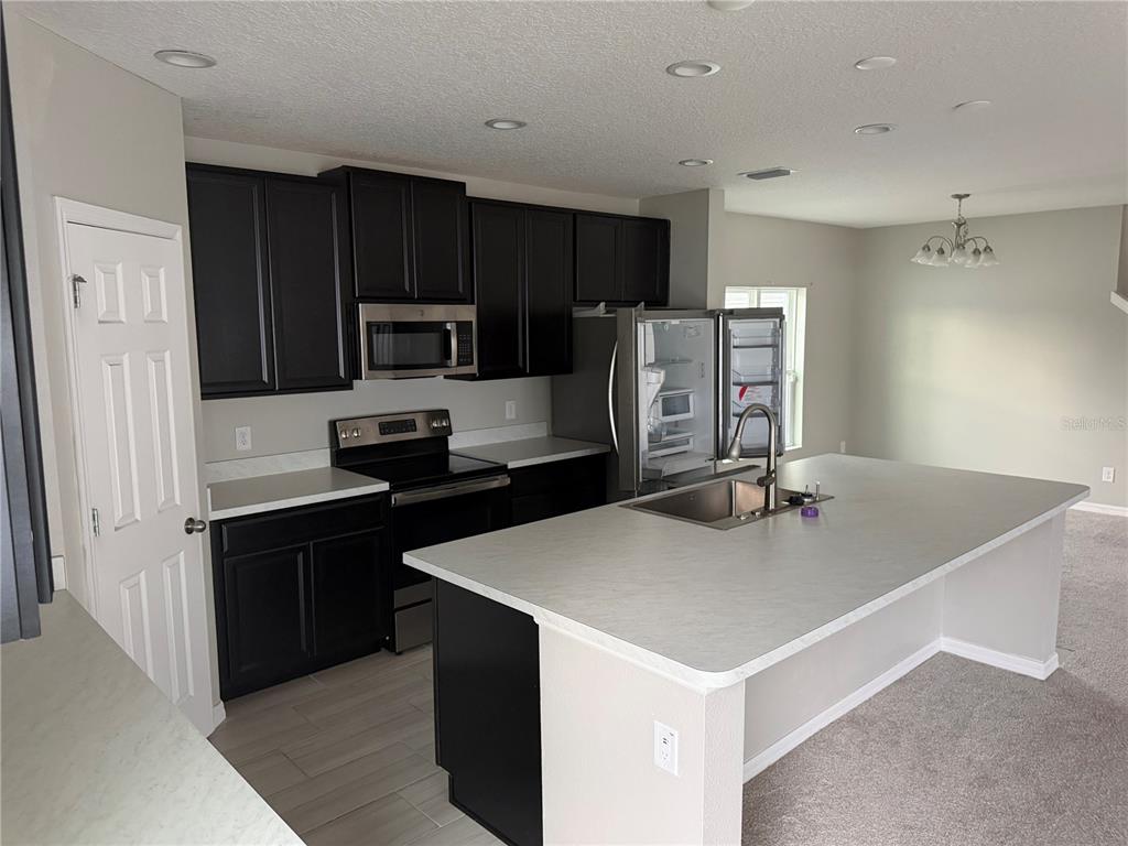 A kitchen features dark cabinets, stainless steel appliances, a large island, and light-colored countertops — 911 AVENAL LANE, DAVENPORT, FL