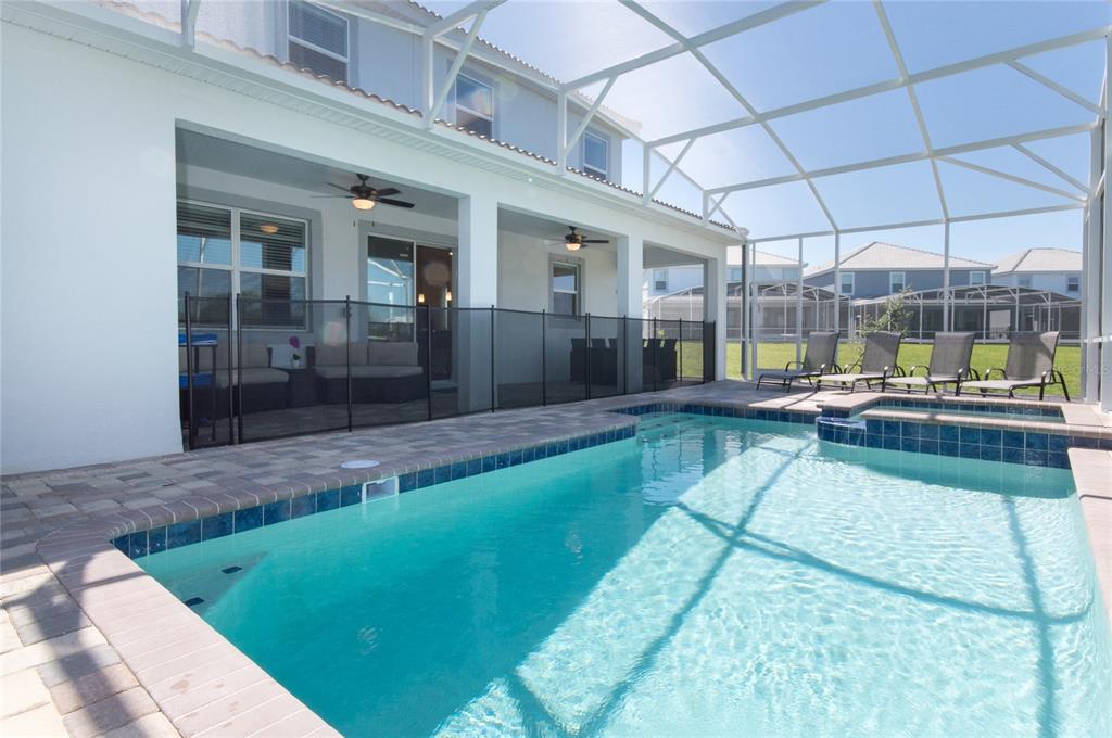 A swimming pool and spa sit on a patio enclosed by a screened lanai — 8847 INTERLOCKING COURT, DAVENPORT, FL