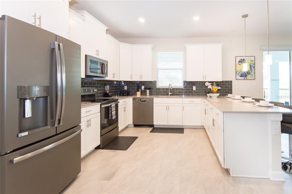 A modern kitchen features white cabinets, stainless steel appliances, a gray tile backsplash, and an island — 8847 INTERLOCKING COURT, DAVENPORT, FL