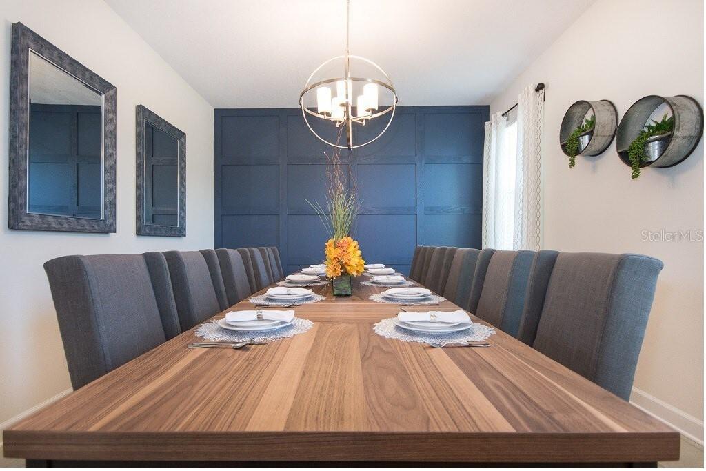 A dining room features a long wooden table, gray upholstered chairs, and a dark blue accent wall — 8847 INTERLOCKING COURT, DAVENPORT, FL
