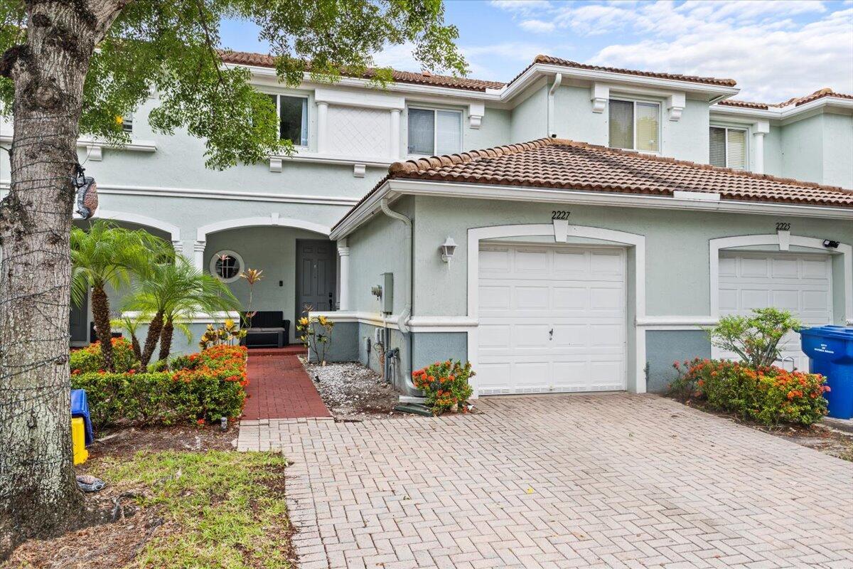A two-story townhouse features a paved driveway, a single-car garage, and a brick walkway — 2227 Oakmont Drive, Riviera Beach FL 33404, RIVIERA BEACH, FL