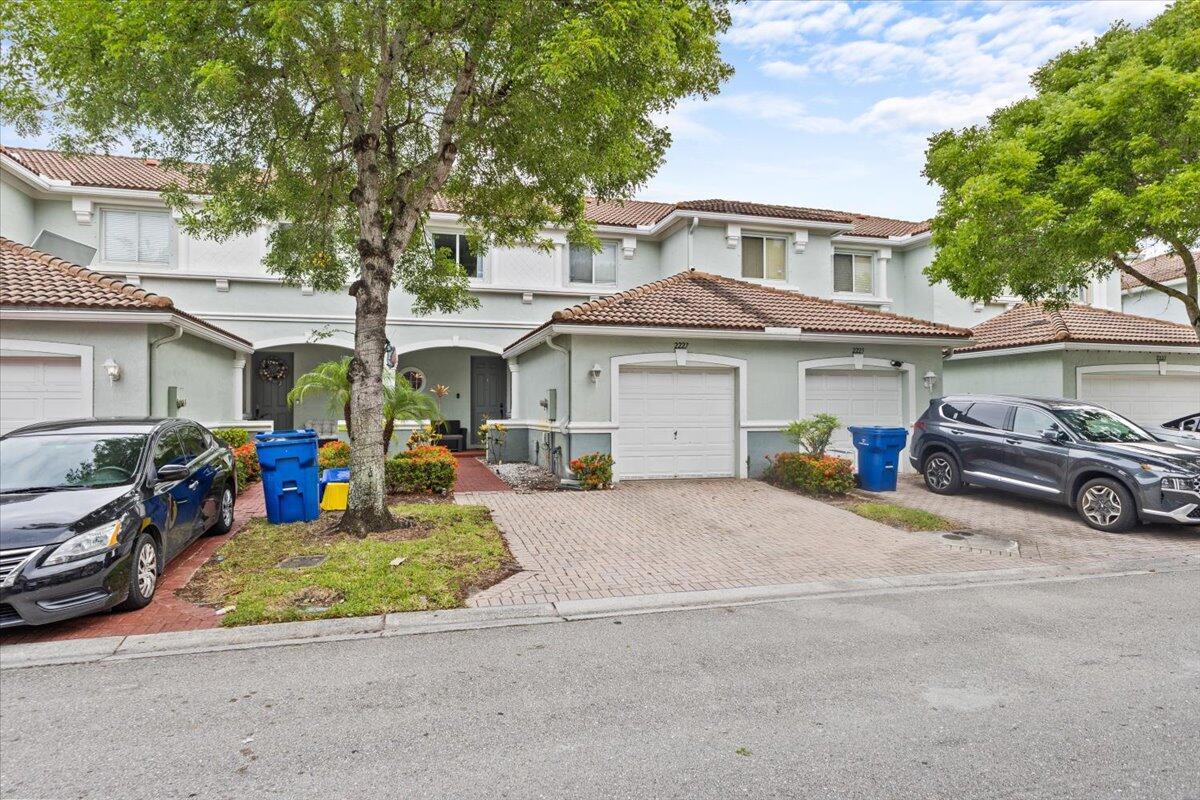 A two-story townhouse exterior features a paved driveway, a garage, and a parked car — 2227 Oakmont Drive, Riviera Beach FL 33404, RIVIERA BEACH, FL