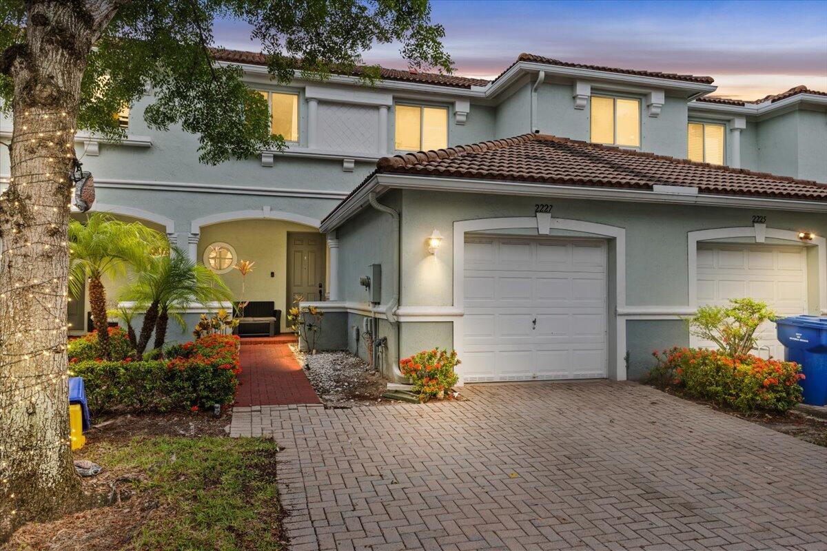 A two-story townhouse with a paved driveway, garage, and a brick walkway leading to the entrance — 2227 Oakmont Drive, Riviera Beach FL 33404, RIVIERA BEACH, FL