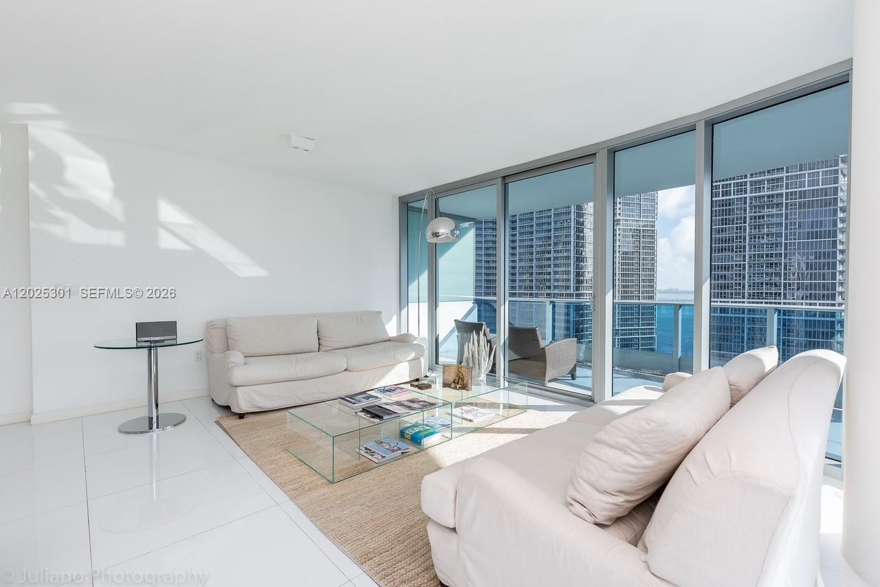 A bright living room features white tile floors, two sofas, a glass coffee table, and floor-to-ceiling windows — 200 Biscayne Boulevard Way # 3102, Miami FL 33131, MIAMI, FL