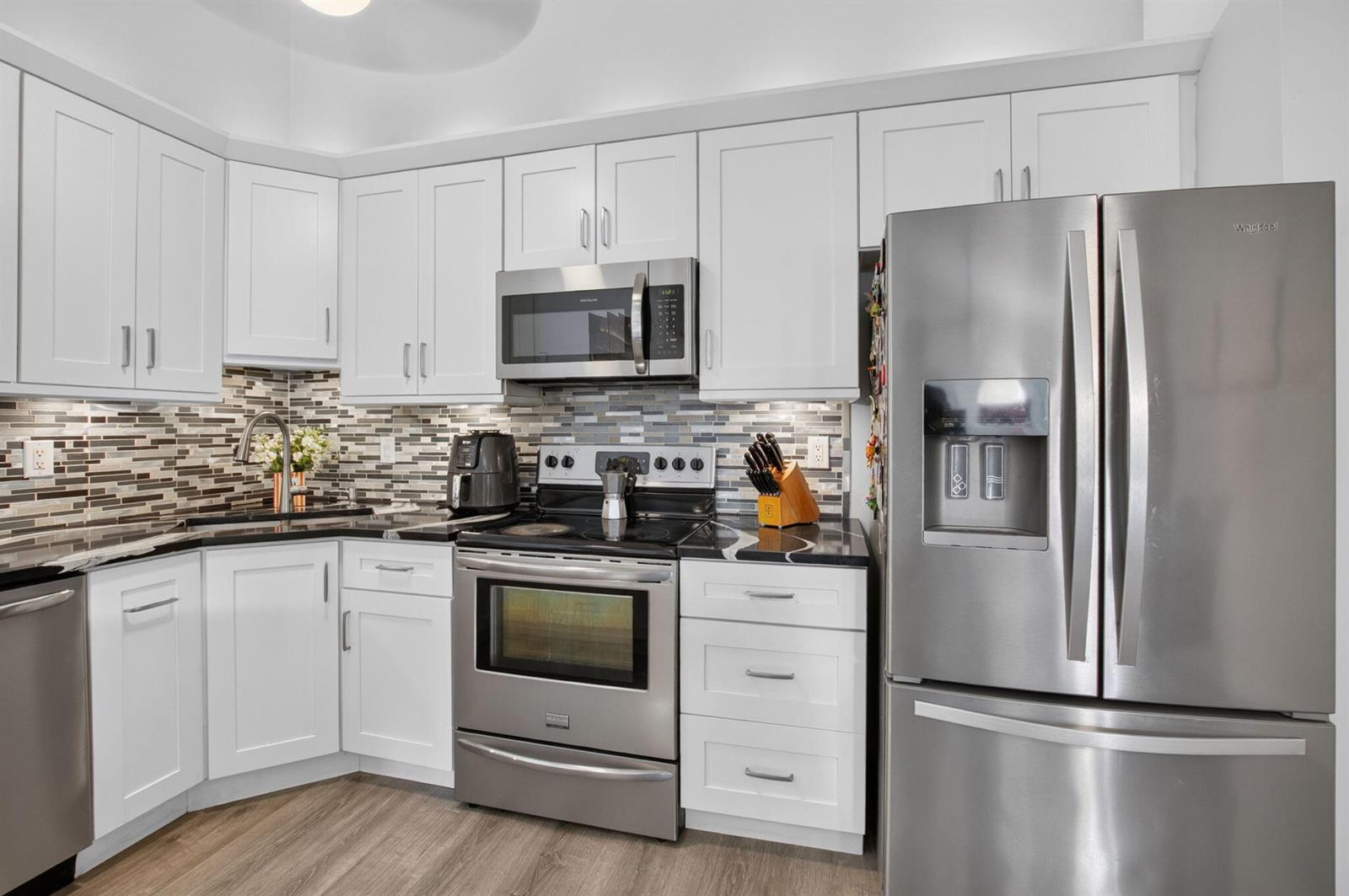 A kitchen features white cabinets, black countertops, stainless steel appliances, and a mosaic tile backsplash — 9622 Boca Gardens Parkway # B, Boca Raton FL 33496, BOCA RATON, FL