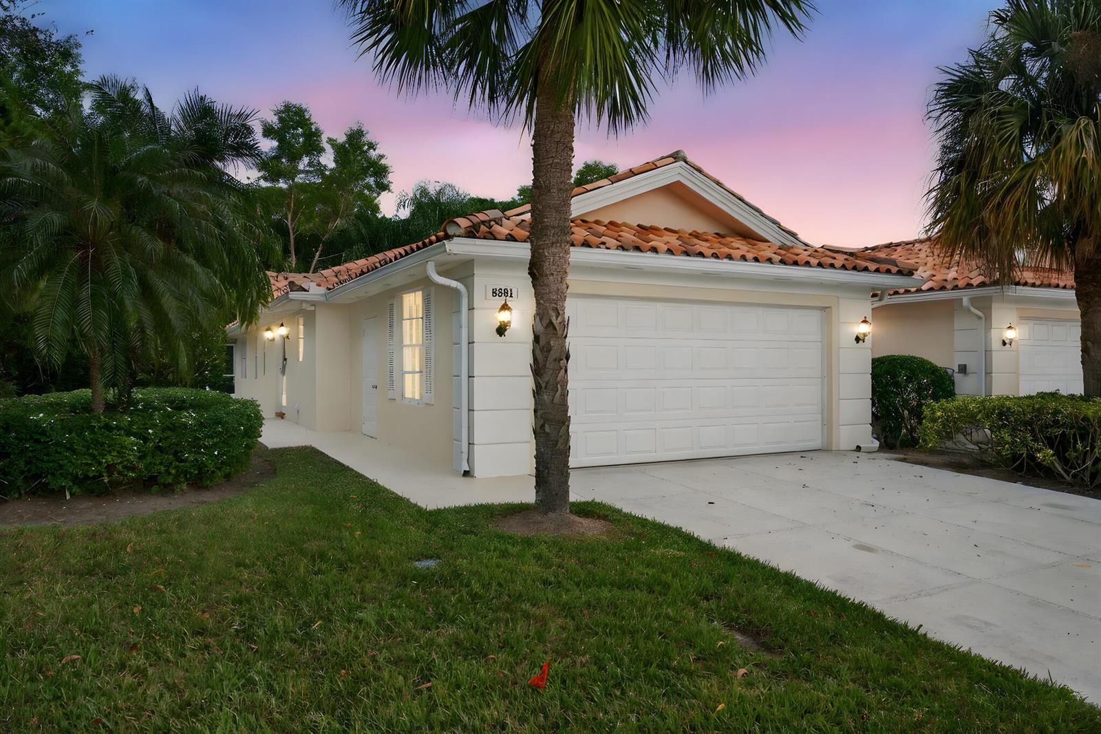 A single-story house with a white garage, tiled roof, and palm trees at dusk — 8381 SE Double Tree Drive, Hobe Sound FL 33455, HOBE SOUND, FL