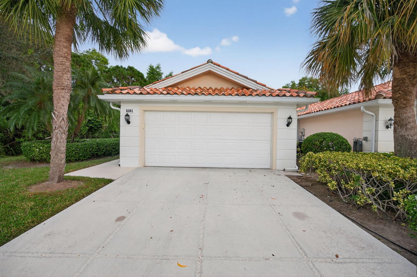 A single-story house exterior features a white garage door, a tiled roof, and palm trees — 8381 SE Double Tree Drive, Hobe Sound FL 33455, HOBE SOUND, FL