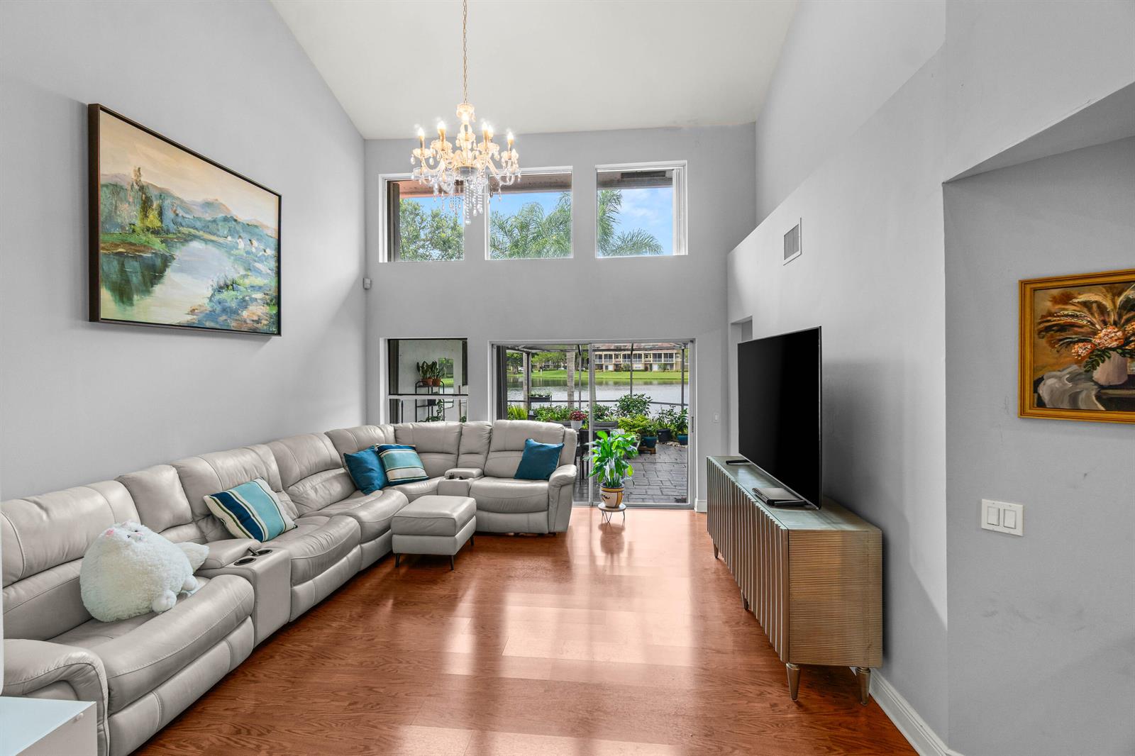 A living room with a vaulted ceiling, light gray walls, a sectional sofa, and lake views — 2011 NW 53rd Street, Boca Raton FL 33496, BOCA RATON, FL