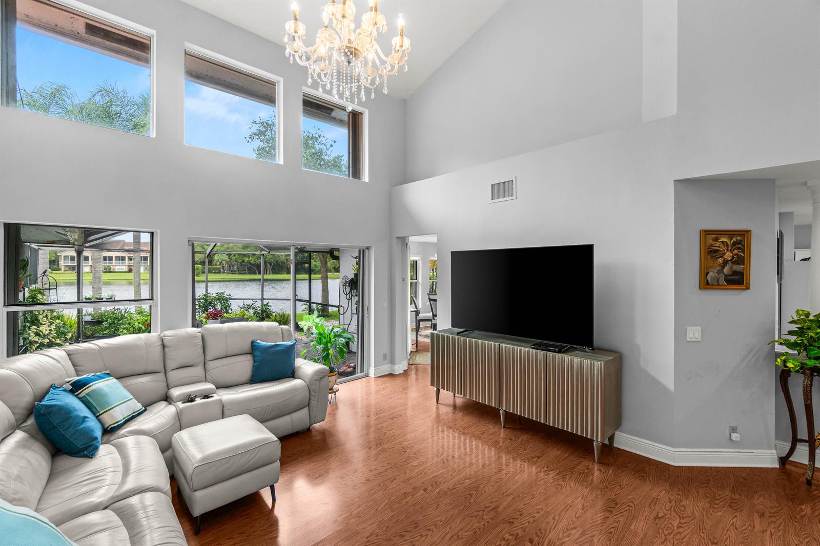 A living room features a vaulted ceiling, chandelier, sectional sofa, and large windows overlooking water — 2011 NW 53rd Street, Boca Raton FL 33496, BOCA RATON, FL