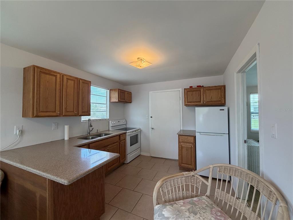 A kitchen features wooden cabinets, a white refrigerator, a stove, and a tiled floor — 8513 HERBISON AVENUE, NORTH PORT, FL