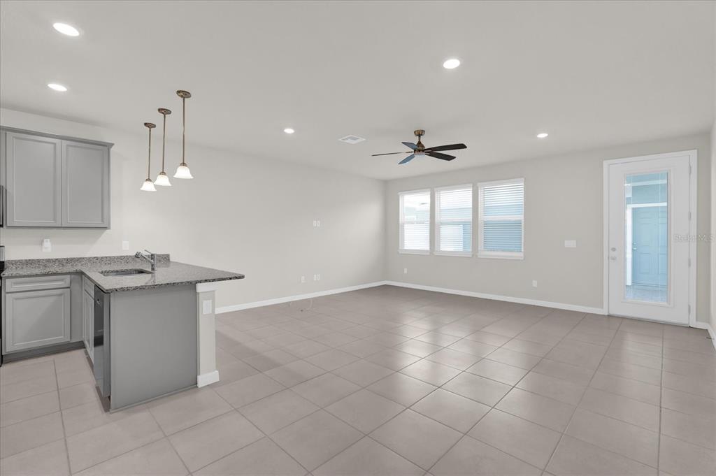 A kitchen with gray cabinets and a granite island opens into a tiled living area — 10877 WOODED ACRE ALLEY, ORLANDO, FL