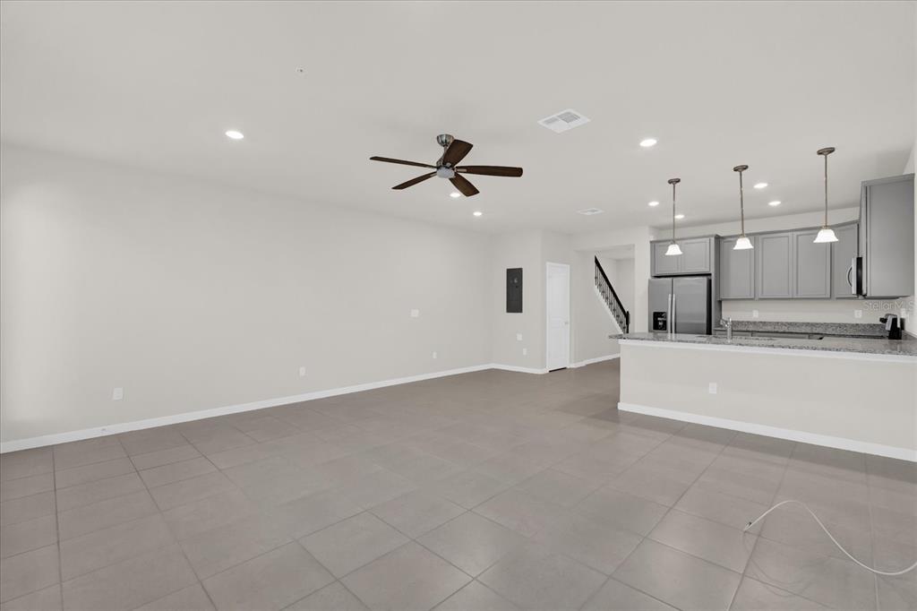 An open-concept living area with gray tile flooring, a ceiling fan, and a modern kitchen — 10877 WOODED ACRE ALLEY, ORLANDO, FL