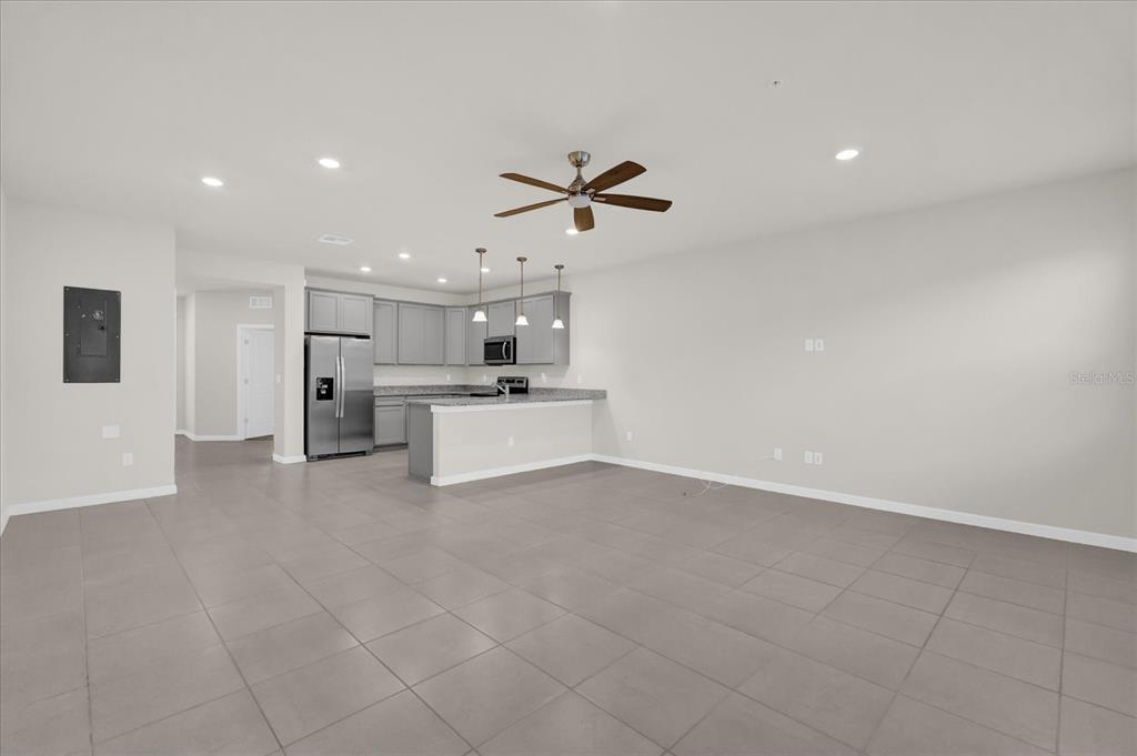 An open-concept kitchen and living area features gray tile flooring, stainless appliances, and pendant lighting — 10877 WOODED ACRE ALLEY, ORLANDO, FL