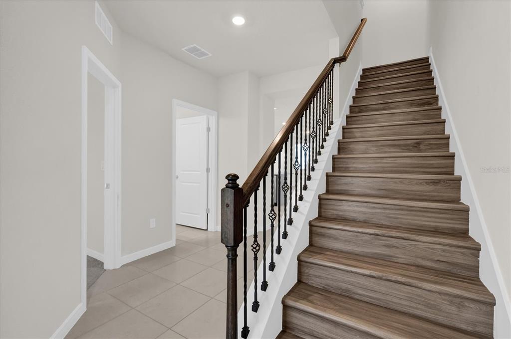 A staircase with wood-look treads and a dark metal railing leads upward in a hallway — 10877 WOODED ACRE ALLEY, ORLANDO, FL