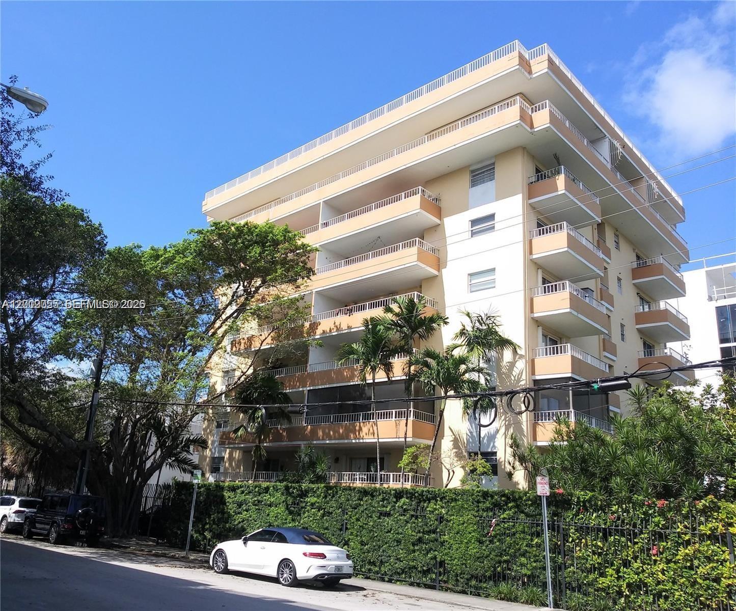 A multi-story apartment building with balconies stands behind a hedge and a parked car — 3304 Virginia St # 3D, Miami FL 33133, MIAMI, FL