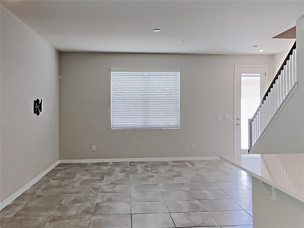 An empty room with tile flooring, a window with blinds, and a staircase — 11912 FOUNDERS STREET, ORLANDO, FL
