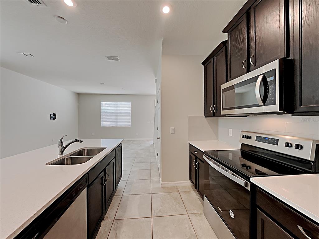 A kitchen features dark wood cabinets, stainless steel appliances, and a white quartz island countertop — 11912 FOUNDERS STREET, ORLANDO, FL