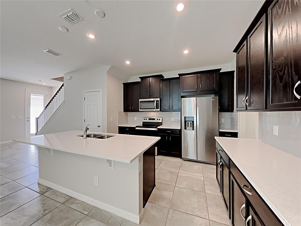 A kitchen features dark wood cabinets, white countertops, a central island, and stainless steel appliances — 11912 FOUNDERS STREET, ORLANDO, FL