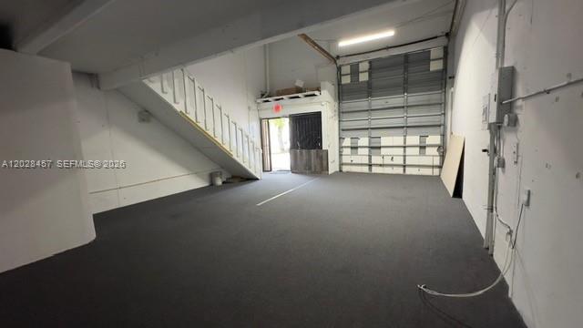 An interior view of a warehouse space with gray carpeting, a staircase, and a roll-up door — 12153 SW 131st Ave, Miami FL 33186, MIAMI, FL