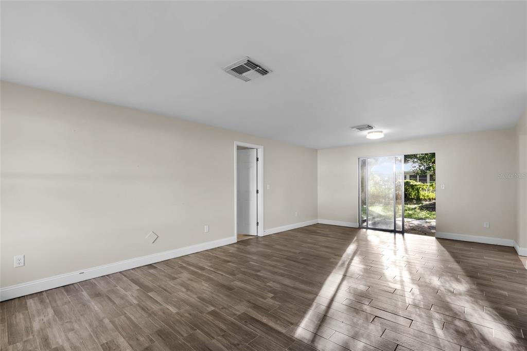 An empty living room features light-colored walls, wood-look tile flooring, and a sliding glass door — 14721 SW 35TH TERRACE ROAD, OCALA, FL