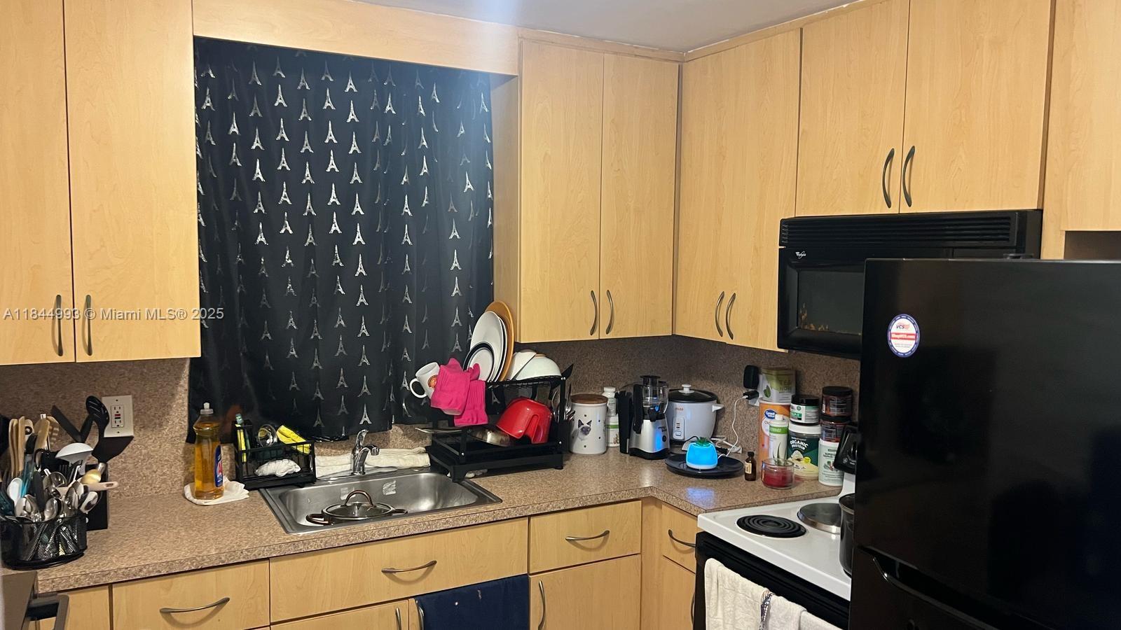 A kitchen features light wood cabinets, a black refrigerator, and a stainless steel sink — 19080 NE 3rd Ct # 307, Miami FL 33179, MIAMI, FL