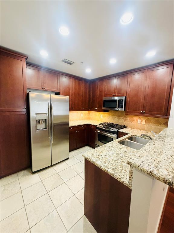 A kitchen features cherry wood cabinets, granite countertops, stainless steel appliances, and tile flooring — 2305 EDGEWATER DRIVE UNIT 1708, ORLANDO, FL