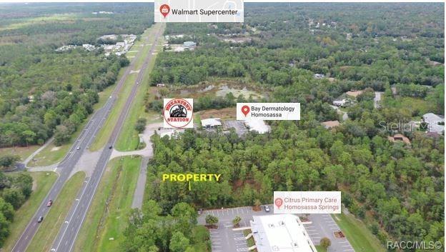 This aerial view shows a wooded lot located between a highway and commercial buildings — 7929 S SUNCOAST BOULEVARD, HOMOSASSA, FL