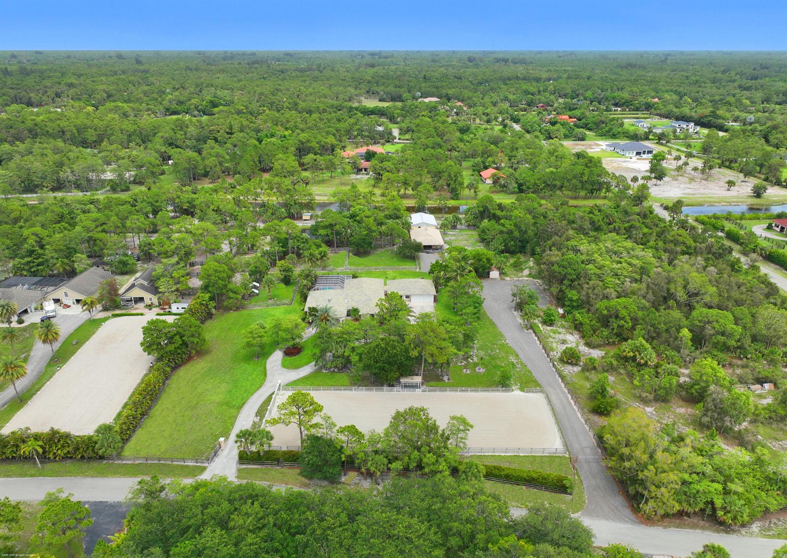 An aerial view shows a residential property with a house, two riding arenas, and trees — 2560 Buck Ridge Trail, Loxahatchee FL 33470, LOXAHATCHEE, FL