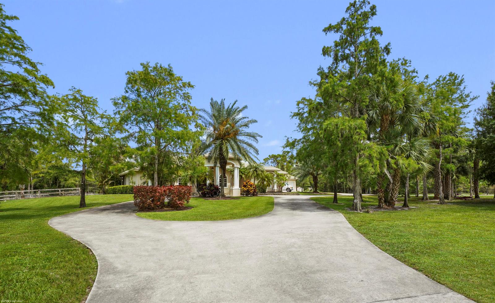 A paved driveway leads to a house with a columned entrance surrounded by lush landscaping — 2560 Buck Ridge Trail, Loxahatchee FL 33470, LOXAHATCHEE, FL