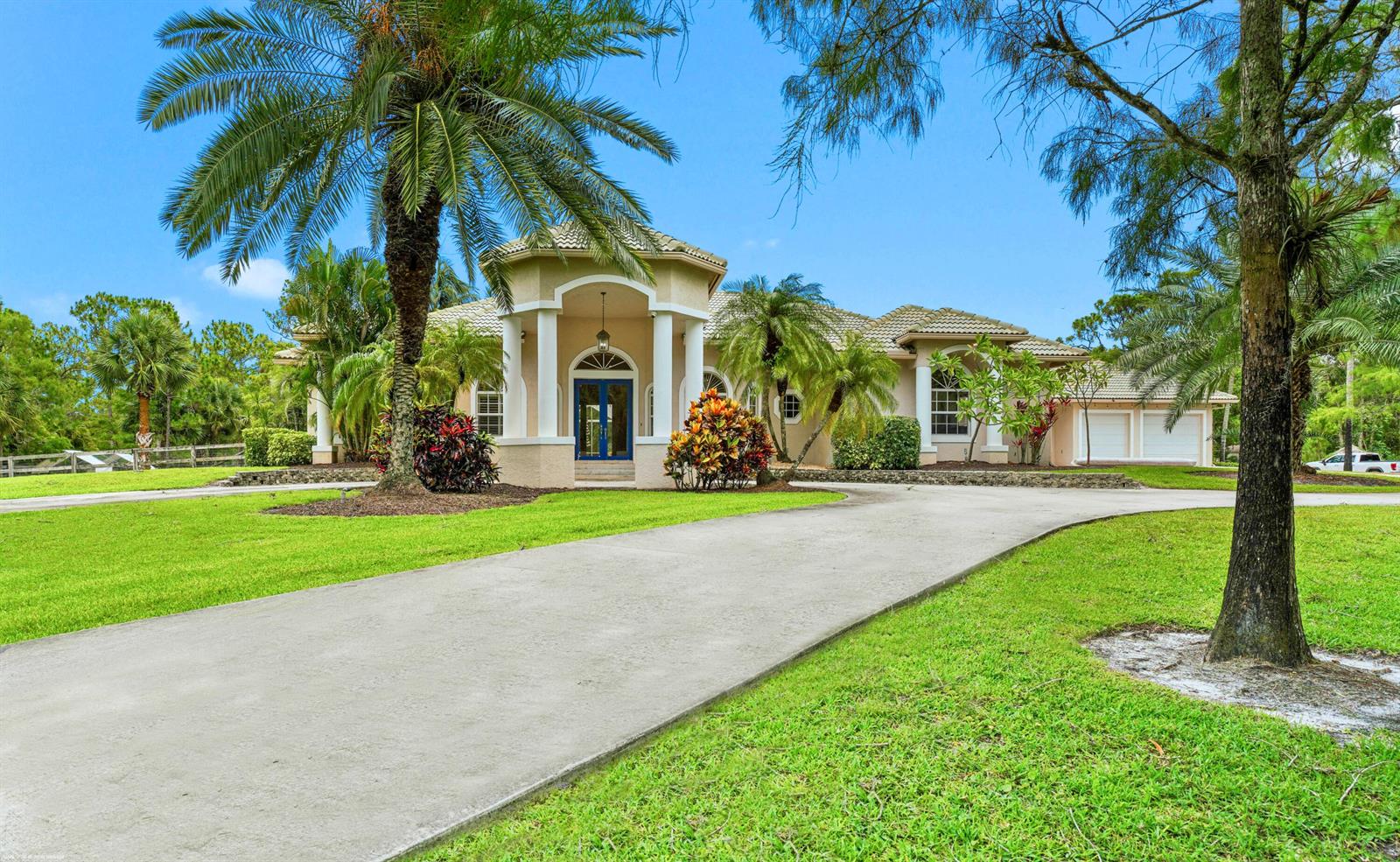 A beige single-story house with a circular entryway, blue double doors, and a concrete driveway — 2560 Buck Ridge Trail, Loxahatchee FL 33470, LOXAHATCHEE, FL