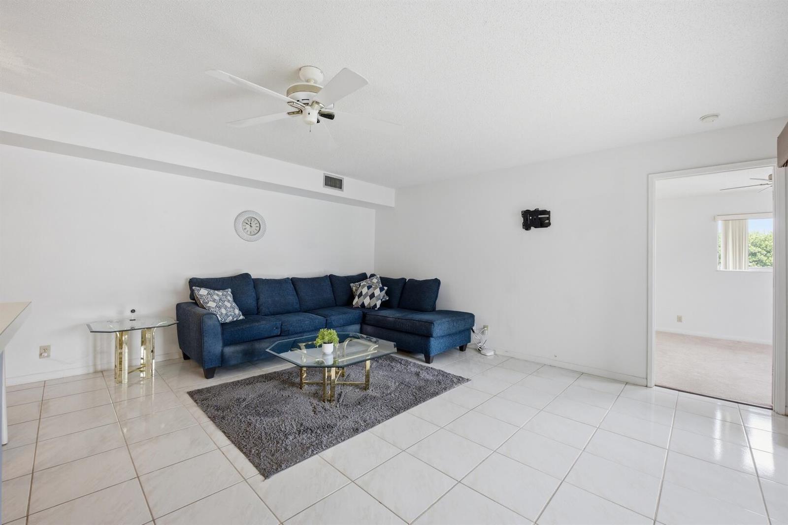 A living room features white tile floors, a blue sectional sofa, and a glass coffee table — 14898 Wedgefield Drive # 208, Delray Beach FL 33446, DELRAY BEACH, FL