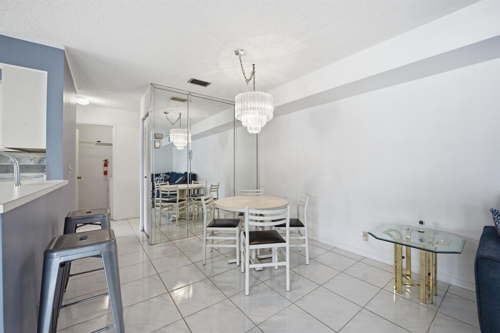 A dining area features a round table, white chairs, a crystal chandelier, and mirrored walls — 14898 Wedgefield Drive # 208, Delray Beach FL 33446, DELRAY BEACH, FL