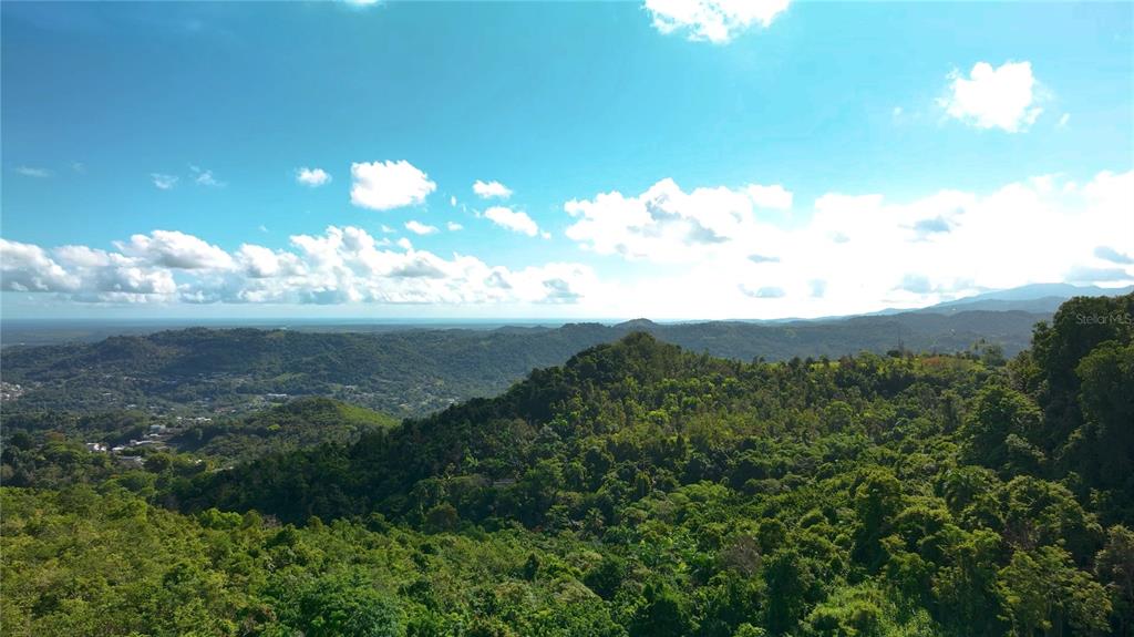 A high-angle view shows a lush, green, mountainous landscape under a bright, cloudy sky — PR181 km 53.3 SECTOR LA SILLA  CARR 941, GURABO, PR