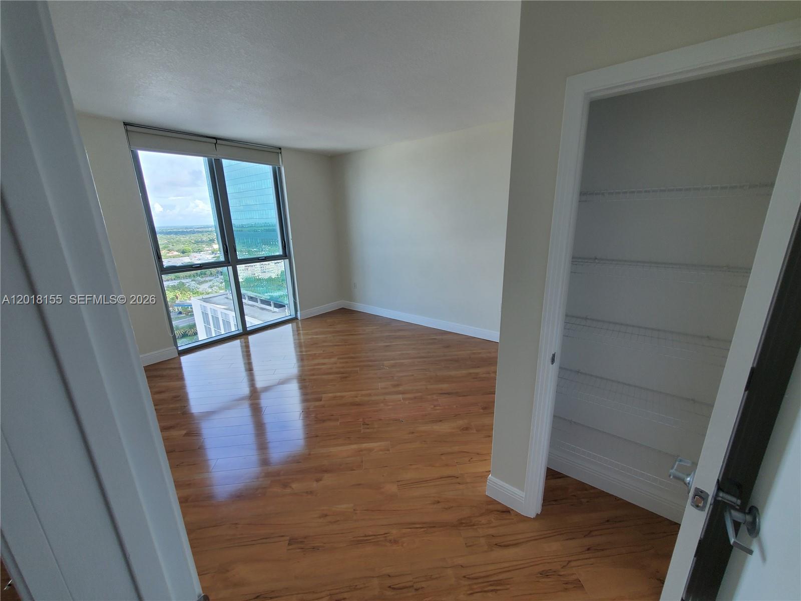 An empty room with wood-look flooring, a closet, and a large window overlooking a city — 9066 SW 73rd Ct # 1808, Miami FL 33156, MIAMI, FL