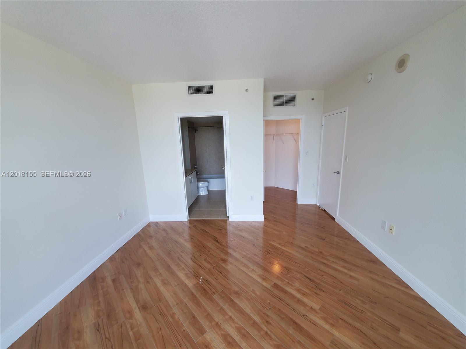 An empty room features wood-look flooring, a bathroom entrance, a walk-in closet, and white walls — 9066 SW 73rd Ct # 1808, Miami FL 33156, MIAMI, FL