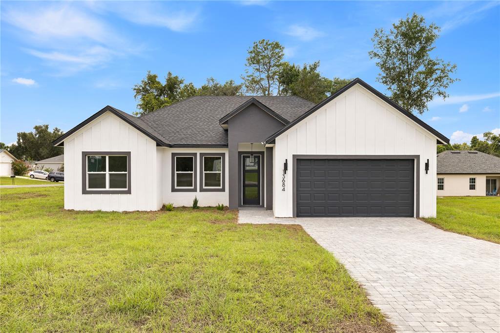 A modern single-story house features white board-and-batten siding, a dark gray garage, and a paved driveway — 13684 SW 43RD CIRCLE, OCALA, FL