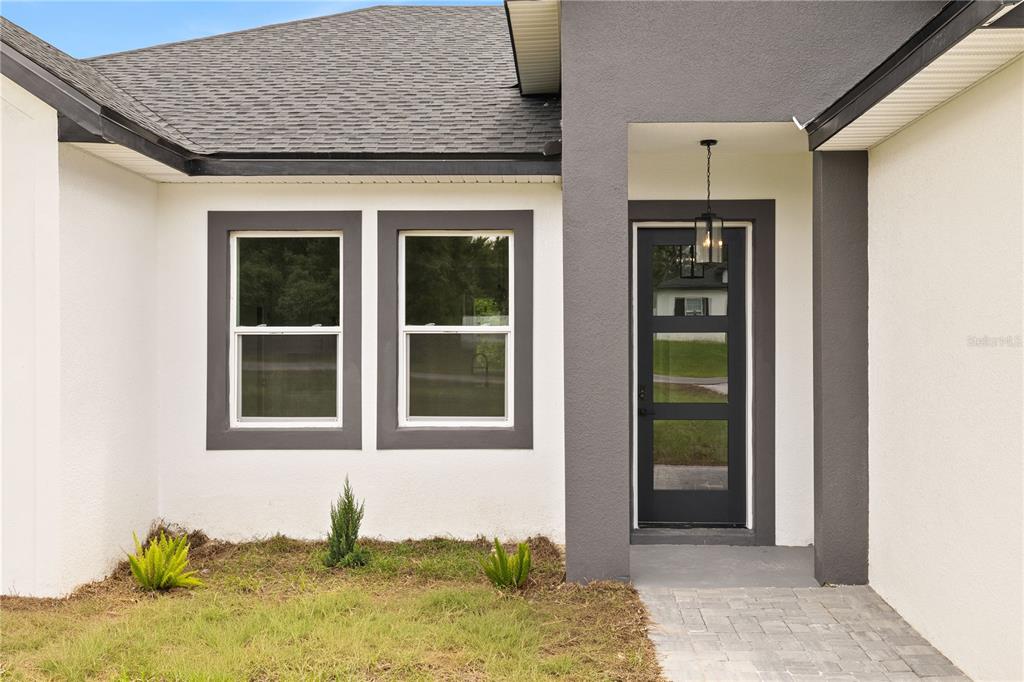A modern home exterior featuring a dark gray entryway, a glass-paneled door, and two windows — 13684 SW 43RD CIRCLE, OCALA, FL
