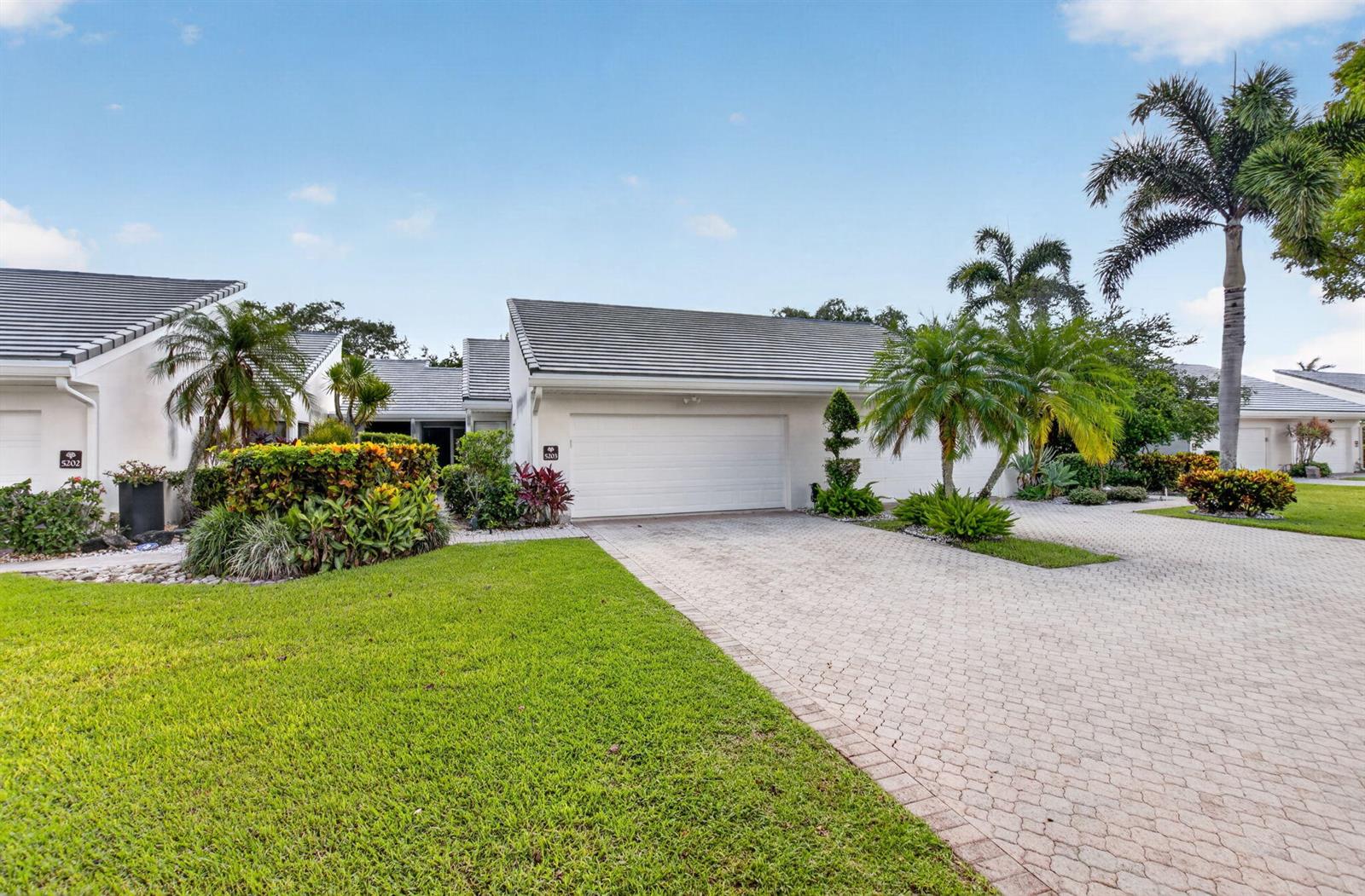 A single-story residential building with a two-car garage, paved driveway, and tropical landscaping — 19950 Sawgrass Lane # 5203, Boca Raton FL 33434, BOCA RATON, FL